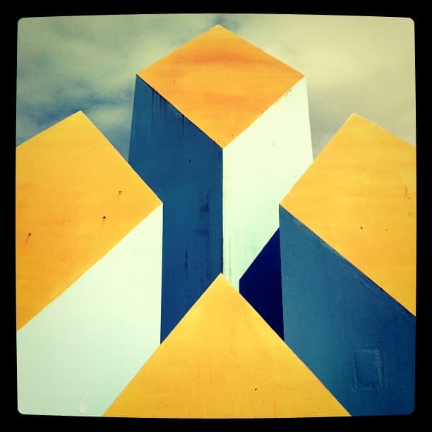 Looking up at a sculpture of angular blocks with yellow tops and blue and white sides
