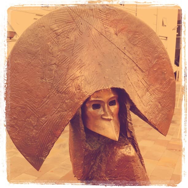Bronze figure in a beaked mask under a wide disc-shaped hat