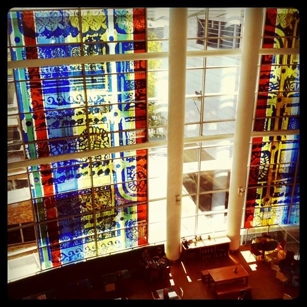 Tall coloured glass panels in red, blue and yellow patterns, seen from an upper floor above a seating area